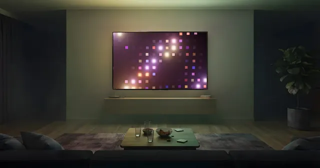 Salón preparado para una fiesta con amigos: sofás, mesa baja con vasos y picoteo, y una gran tele de pared que ilumina la sala con cuadrados de luz de colores.