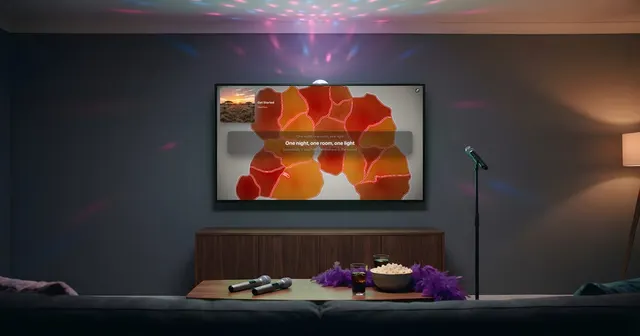 Salón preparado para un karaoke: un micrófono de pie, dos micrófonos y una boa morada sobre la mesa baja, palomitas, una bola de espejos en el techo y la tele mostrando la letra de una canción.